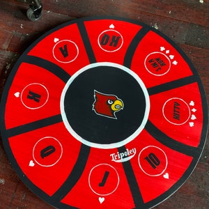 May include: A red and black circular game board with a cardinal mascot in the center. The board has numbers and playing card symbols around the edge. The text "Tripoley" is printed on the board.