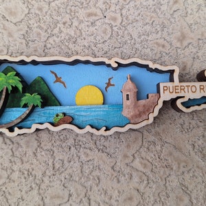 以下が含まれることがあります： 青い空、ヤシの木、黄色い太陽、要塞、そして右側に「プエルトリコ」の文字が書かれた、プエルトリコ島の木製の切り抜きです。