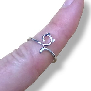 May include: A silver ring with a cat design. The cat's tail wraps around the finger.