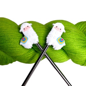 May include: Two silver knitting needles with white llama-shaped stitch markers. The needles are crossed and resting on a ball of bright green yarn.