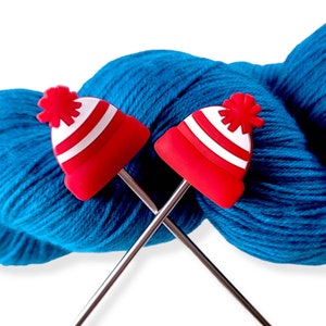 May include: Two red and white knit hat-shaped knitting needles with a blue ball of yarn.