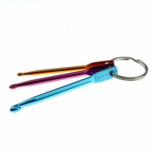 May include: A set of three colorful crochet hooks attached to a silver key ring. The hooks are blue, pink, and orange. The largest hook is labeled "5 mm".