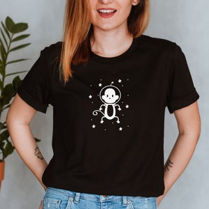 May include: A black t-shirt with a white graphic of a monkey wearing an astronaut helmet and floating in space. The monkey is surrounded by white stars.