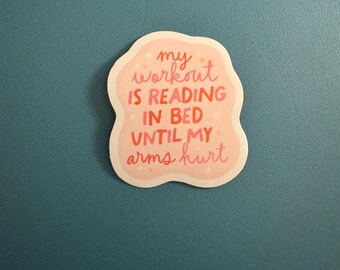 May include: A sticker with a light pink background and a white border. The sticker has the text "my workout is reading in bed until my arms hurt" in a mix of pink and red fonts. Small star shapes are scattered around the text.