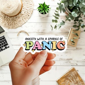 May include: A die-cut vinyl sticker featuring the text ANXIETY WITH A SPARKLE OF PANIC. The word PANIC is written in large, colorful, bubble-style letters in shades of light green, pink, blue, yellow, and orange, accented with small yellow stars.