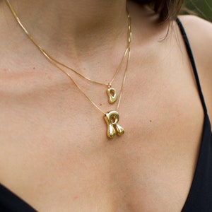 May include: Two gold necklaces with a letter 'D' pendant and a letter 'R' pendant. The 'R' pendant is a unique, abstract design.