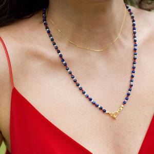 May include: A necklace with blue, white, and red beads. The necklace has a gold clasp.