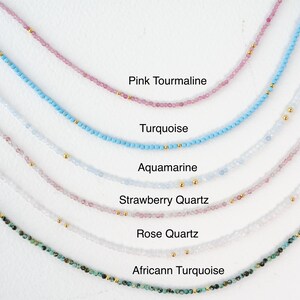 K&ouml;nnte beinhalten: Eine Sammlung zarter Halsketten mit verschiedenen Edelsteinen, darunter rosa Turmalin, T&uuml;rkis, Aquamarin, Erdbeerquarz, Rosenquarz und afrikanischer T&uuml;rkis. Jede Halskette besteht aus kleinen Perlen und goldenen Akzenten.