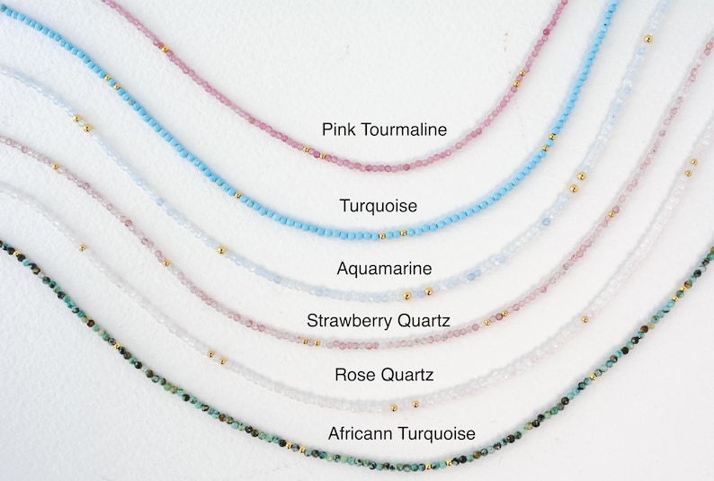 K&ouml;nnte beinhalten: Eine Sammlung zarter Halsketten mit verschiedenen Edelsteinen, darunter rosa Turmalin, T&uuml;rkis, Aquamarin, Erdbeerquarz, Rosenquarz und afrikanischer T&uuml;rkis. Jede Halskette besteht aus kleinen Perlen und goldenen Akzenten.