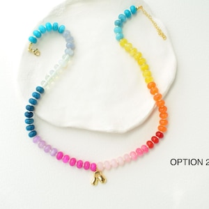 May include: A colorful beaded necklace with a gradient of colors, from blue to red. The necklace has a gold clasp and a small gold charm. The necklace is labeled "OPTION 2".