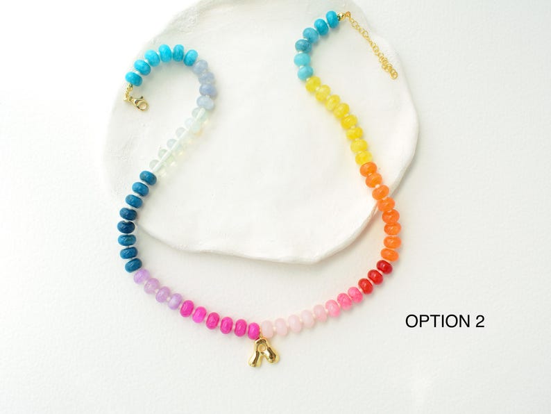 May include: A colorful beaded necklace with a gradient of colors, from blue to red. The necklace has a gold clasp and a small gold charm. The necklace is labeled "OPTION 2".