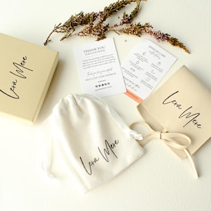 May include: A cream-colored jewelry box, pouch, and bag with the handwritten brand name "Lera Mere" in black. The set includes care instructions and a thank you card. A sprig of dried flowers adds a natural accent.