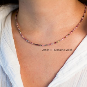 K&ouml;nnte beinhalten: Eine zarte Halskette aus kleinen, bunten Turmalinperlen. Die Halskette wird von einem Model getragen, das ein wei&szlig;es Hemd tr&auml;gt. Der Text "Option1: Tourmaline Mixed" ist unterhalb der Halskette sichtbar.