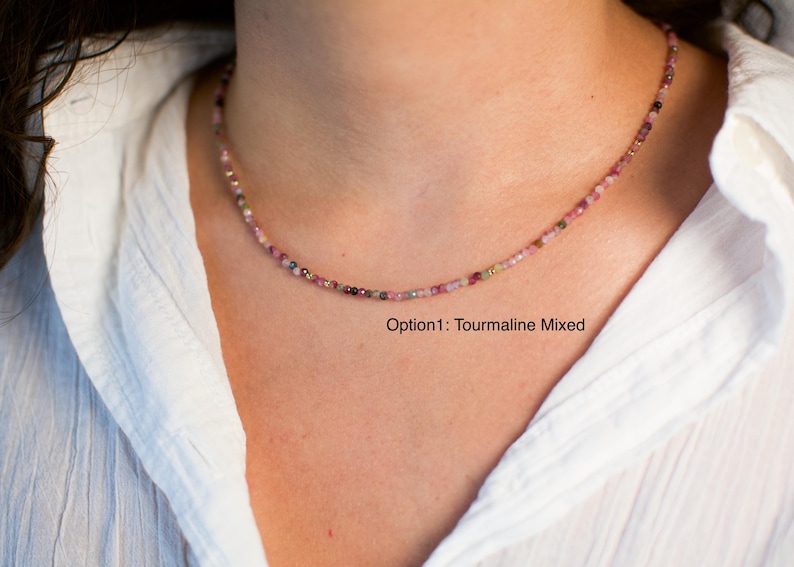 K&ouml;nnte beinhalten: Eine zarte Halskette aus kleinen, bunten Turmalinperlen. Die Halskette wird von einem Model getragen, das ein wei&szlig;es Hemd tr&auml;gt. Der Text "Option1: Tourmaline Mixed" ist unterhalb der Halskette sichtbar.