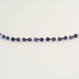 May include: A delicate necklace made with small blue, red, and white beads. The necklace is made with a simple design and is perfect for everyday wear.
