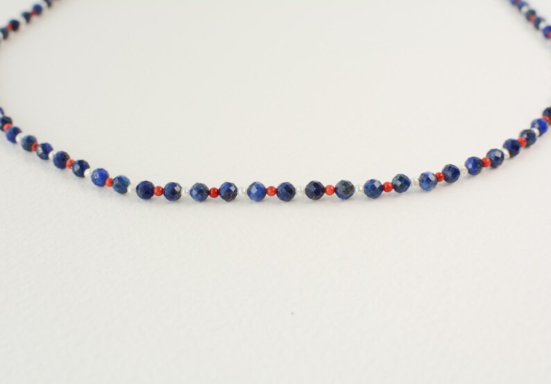 May include: A delicate necklace made with small blue, red, and white beads. The necklace is made with a simple design and is perfect for everyday wear.