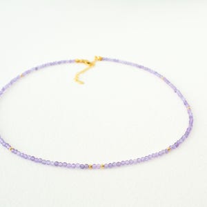 May include: A delicate purple amethyst beaded necklace with gold accents. The necklace is made with small, round beads and has a simple, elegant design.