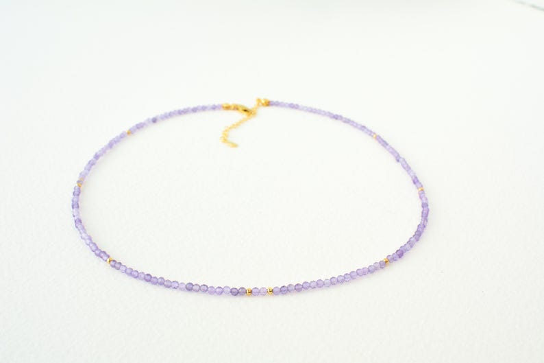 May include: A delicate purple amethyst beaded necklace with gold accents. The necklace is made with small, round beads and has a simple, elegant design.