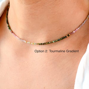 K&ouml;nnte beinhalten: Eine zarte Halskette mit einem Farbverlauf aus rosa, gr&uuml;nen und goldenen Turmalinperlen. Die Halskette wird von einem Model getragen, das ein wei&szlig;es Hemd tr&auml;gt. Der Text "Option 2: Tourmaline Gradient" befindet sich unterhalb der Halskette.