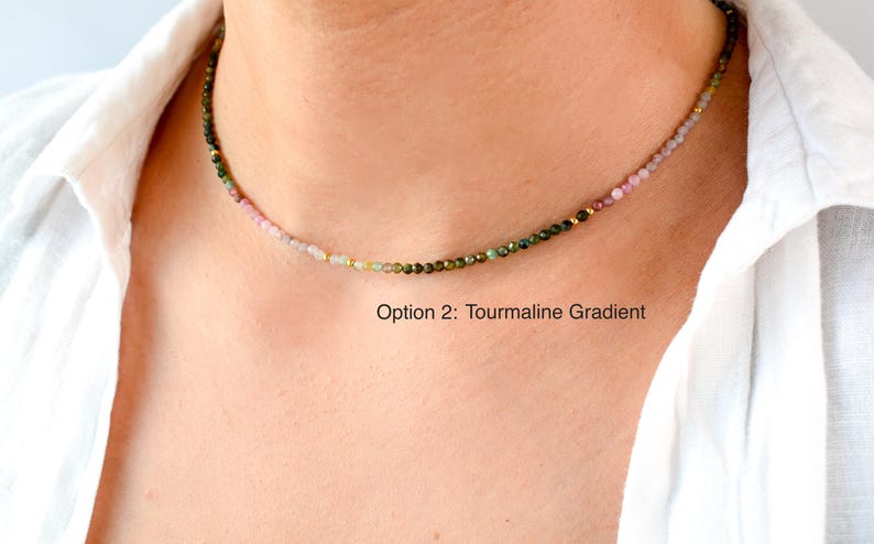 K&ouml;nnte beinhalten: Eine zarte Halskette mit einem Farbverlauf aus rosa, gr&uuml;nen und goldenen Turmalinperlen. Die Halskette wird von einem Model getragen, das ein wei&szlig;es Hemd tr&auml;gt. Der Text "Option 2: Tourmaline Gradient" befindet sich unterhalb der Halskette.