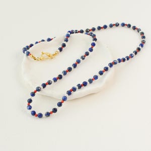 May include: A necklace made of blue, red, and white beads. The necklace is on a white surface.