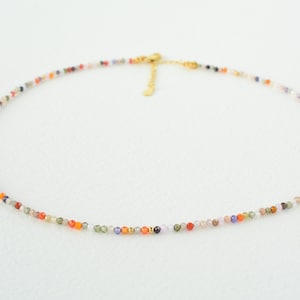 Puede incluir: Un delicado collar de cadena dorada con peque&ntilde;as cuentas de piedras preciosas de colores. El collar est&aacute; hecho de peque&ntilde;as cuentas multicolores, creando un look vibrante y llamativo.