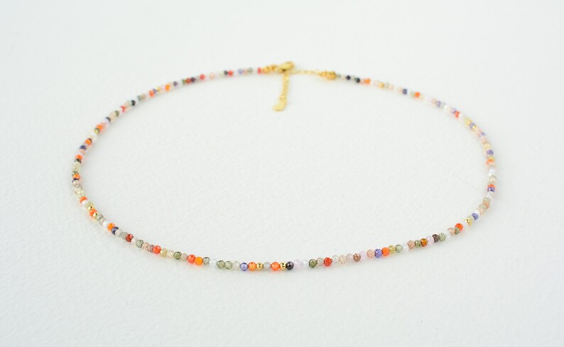 Puede incluir: Un delicado collar de cadena dorada con peque&ntilde;as cuentas de piedras preciosas de colores. El collar est&aacute; hecho de peque&ntilde;as cuentas multicolores, creando un look vibrante y llamativo.