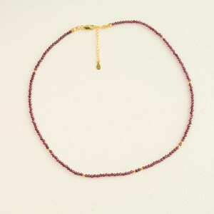 May include: A delicate gold chain necklace with small, dark red garnet beads.