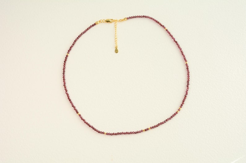 May include: A delicate gold chain necklace with small, dark red garnet beads.