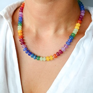 May include: A colorful beaded necklace with a rainbow of colors, including red, orange, yellow, green, blue, and purple. The necklace is worn against a white shirt.