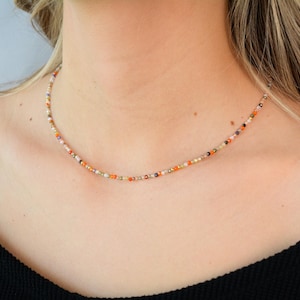 Puede incluir: Un delicado collar choker hecho con peque&ntilde;as cuentas de colores en tonos naranja, blanco y marr&oacute;n.