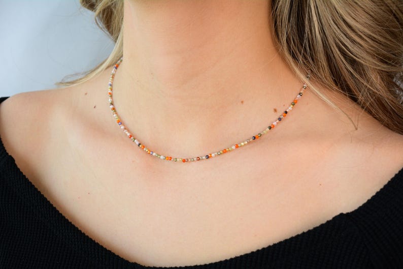 Puede incluir: Un delicado collar choker hecho con peque&ntilde;as cuentas de colores en tonos naranja, blanco y marr&oacute;n.