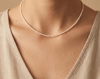 May include: A delicate necklace composed of a single strand of small, round, white pearls. The pearls are uniform in size and shape, creating a continuous, smooth circle that rests against the base of the neck. The necklace features a simple design.