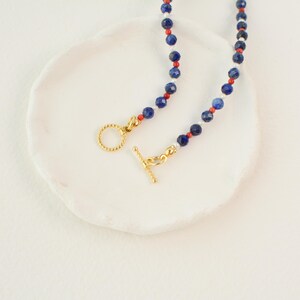 May include: A necklace with blue, red, and white beads and a gold clasp.