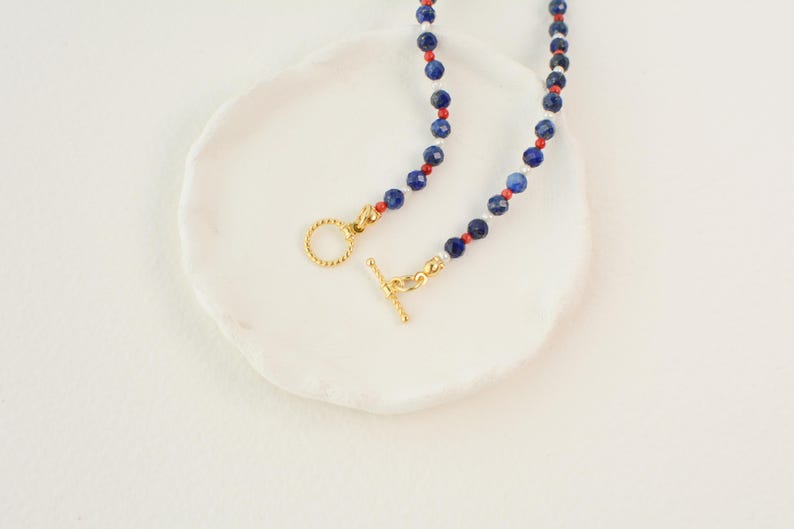May include: A necklace with blue, red, and white beads and a gold clasp.