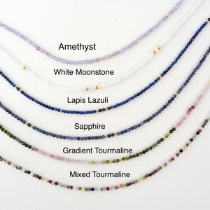 Puede incluir: Primer plano de seis collares diferentes hechos con cuentas de piedras preciosas. Los collares est&aacute;n dispuestos en una fila de arriba a abajo, con el collar superior de amatista, seguido de piedra lunar blanca, lapisl&aacute;zuli, zafiro, turmalina degradada y turmalina mixta.