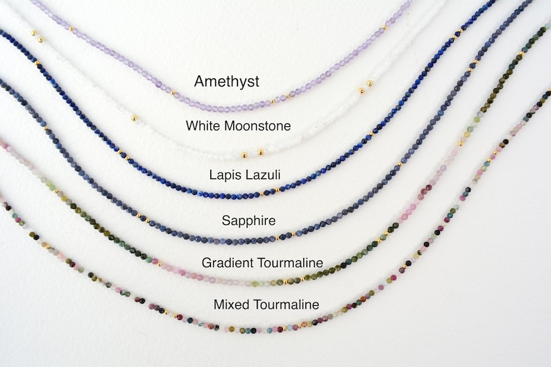 Puede incluir: Primer plano de seis collares diferentes hechos con cuentas de piedras preciosas. Los collares est&aacute;n dispuestos en una fila de arriba a abajo, con el collar superior de amatista, seguido de piedra lunar blanca, lapisl&aacute;zuli, zafiro, turmalina degradada y turmalina mixta.