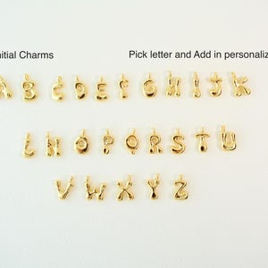 May include: Gold-colored initial charms arranged on a white surface. The image includes the alphabet from A to Z, with the text "Initial Charms" and "Pick letter and Add in personalization area".