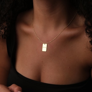 Peut inclure: Un collier doré avec un pendentif rectangulaire portant l'inscription "I love you" en écriture fine. Le collier est porté sur un cou, sur un fond sombre, mettant en valeur la couleur dorée.