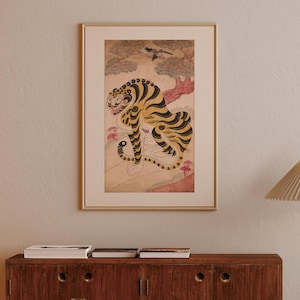 May include: Framed artwork depicting a stylized tiger with yellow and black stripes, set against a landscape with trees and a bird. The artwork has a vintage aesthetic, with a warm colour palette and a gold frame. The tiger is the focal point.