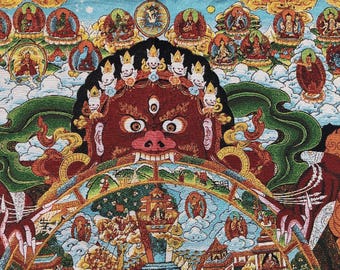 May include: A colorful tapestry featuring a central, fierce-looking red face with a third eye and a crown of skulls. The tapestry includes detailed illustrations of figures, buildings, and text, set against a backdrop of clouds and a blue sky.