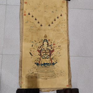 Puede incluir: Una pintura en rollo asiática vintage que presenta una figura central con múltiples brazos, rodeada de figuras más pequeñas y motivos de nubes. La obra de arte está realizada en tonos apagados de beige, azul y rojo, con detalles intrincados e imágenes tradicionales.
