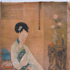 Puede incluir: Pintura asiática antigua que representa a una mujer con vestimenta tradicional. Está sentada, con la mano en la barbilla. A su derecha hay una mesa con un jarrón con flores rosas y otros objetos. El fondo es de un tono cálido y apagado.