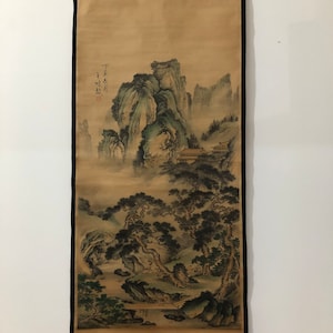 May include: A vintage Asian scroll painting depicting a mountainous landscape with trees, buildings, and a body of water. The artwork features muted tones of green, brown, and beige. The scroll is framed with black borders and a wooden dowel at the bottom.