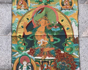 May include: A colorful tapestry featuring a central figure surrounded by other figures in a spiritual setting. The tapestry has a teal background with gold, red, and green accents. The central figure is seated with a halo, and other figures are in the clouds.