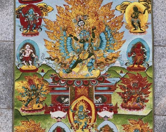 May include: A rectangular tapestry featuring a central deity with multiple arms and a blue complexion, surrounded by other figures in various poses. The tapestry has a light blue background with gold, red, and green accents, depicting a religious or spiritual theme.