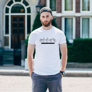 May include: White t-shirt with a black graphic of hands signing "to the greatest".