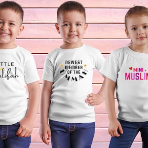 May include: Three white t-shirts with different designs. The first shirt has a yellow crescent moon and the text "LITTLE khalifah". The second shirt has a yellow star and the text "NEWEST MEMBER OF THE UMMAH". The third shirt has a pink heart and the text "MINI MUSLIM".