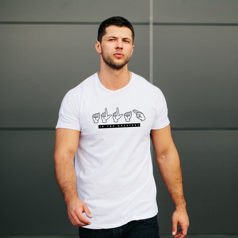 May include: White t-shirt with a black graphic of five hands signing "God is the greatest" in American Sign Language.