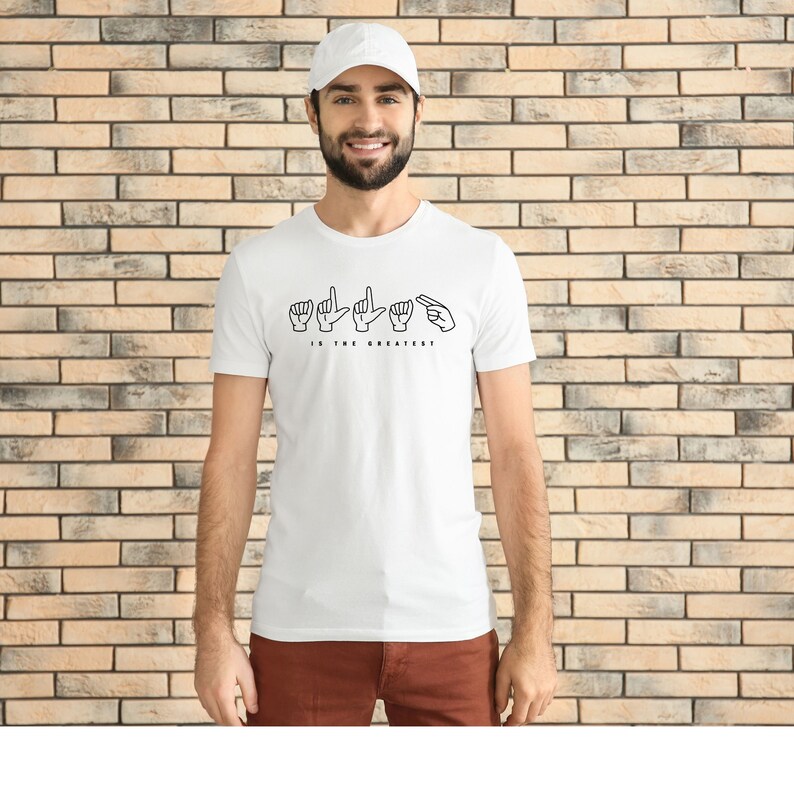 May include: White t-shirt with a black graphic of hands signing "Is the greatest?" in American Sign Language.